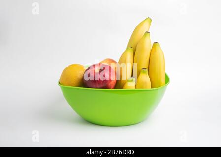Eine leuchtend grüne Plastikschale mit kunstvoll angeordneten frischen und reifen Früchten wie Äpfeln, Bananen, Orangen und anderen auf einem einfarbigen weißen Hintergrund. Stockfoto