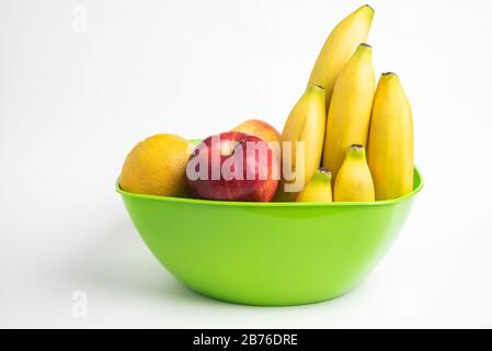 Eine leuchtend grüne Plastikschale mit kunstvoll angeordneten frischen und reifen Früchten wie Äpfeln, Bananen, Orangen und anderen auf einem einfarbigen weißen Hintergrund. Stockfoto