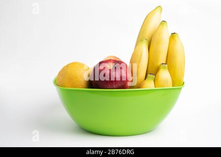 Eine leuchtend grüne Plastikschale mit kunstvoll angeordneten frischen und reifen Früchten wie Äpfeln, Bananen, Orangen und anderen auf einem einfarbigen weißen Hintergrund. Stockfoto