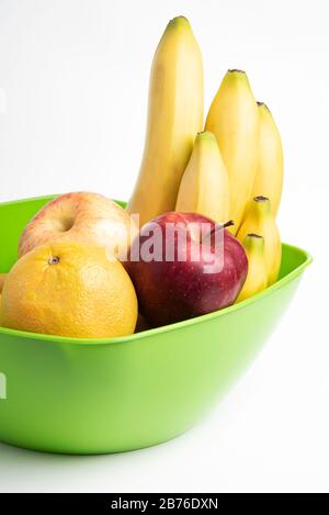 Eine leuchtend grüne Plastikschale mit kunstvoll angeordneten frischen und reifen Früchten wie Äpfeln, Bananen, Orangen und anderen auf einem einfarbigen weißen Hintergrund. Stockfoto