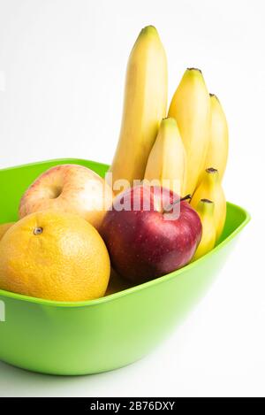 Eine leuchtend grüne Plastikschale mit kunstvoll angeordneten frischen und reifen Früchten wie Äpfeln, Bananen, Orangen und anderen auf einem einfarbigen weißen Hintergrund. Stockfoto