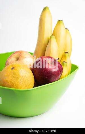 Eine leuchtend grüne Plastikschale mit kunstvoll angeordneten frischen und reifen Früchten wie Äpfeln, Bananen, Orangen und anderen auf einem einfarbigen weißen Hintergrund. Stockfoto