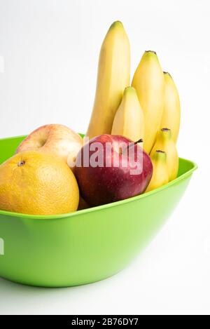 Eine leuchtend grüne Plastikschale mit kunstvoll angeordneten frischen und reifen Früchten wie Äpfeln, Bananen, Orangen und anderen auf einem einfarbigen weißen Hintergrund. Stockfoto