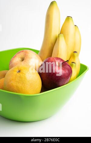 Eine leuchtend grüne Plastikschale mit kunstvoll angeordneten frischen und reifen Früchten wie Äpfeln, Bananen, Orangen und anderen auf einem einfarbigen weißen Hintergrund. Stockfoto