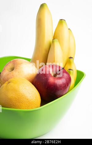 Eine leuchtend grüne Plastikschale mit kunstvoll angeordneten frischen und reifen Früchten wie Äpfeln, Bananen, Orangen und anderen auf einem einfarbigen weißen Hintergrund. Stockfoto