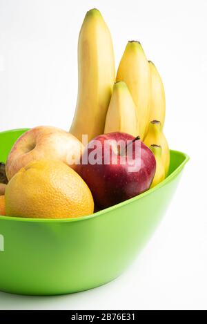 Eine leuchtend grüne Plastikschale mit kunstvoll angeordneten frischen und reifen Früchten wie Äpfeln, Bananen, Orangen und anderen auf einem einfarbigen weißen Hintergrund. Stockfoto