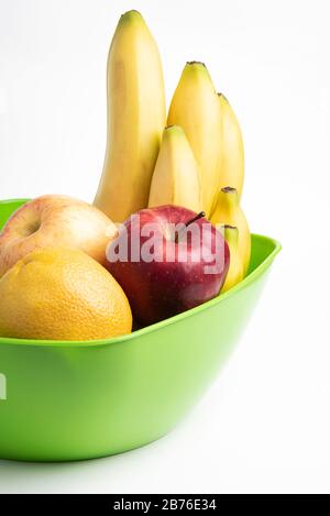 Eine leuchtend grüne Plastikschale mit kunstvoll angeordneten frischen und reifen Früchten wie Äpfeln, Bananen, Orangen und anderen auf einem einfarbigen weißen Hintergrund. Stockfoto