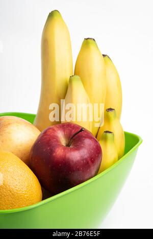 Eine leuchtend grüne Plastikschale mit kunstvoll angeordneten frischen und reifen Früchten wie Äpfeln, Bananen, Orangen und anderen auf einem einfarbigen weißen Hintergrund. Stockfoto