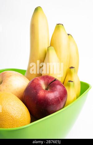 Eine leuchtend grüne Plastikschale mit kunstvoll angeordneten frischen und reifen Früchten wie Äpfeln, Bananen, Orangen und anderen auf einem einfarbigen weißen Hintergrund. Stockfoto