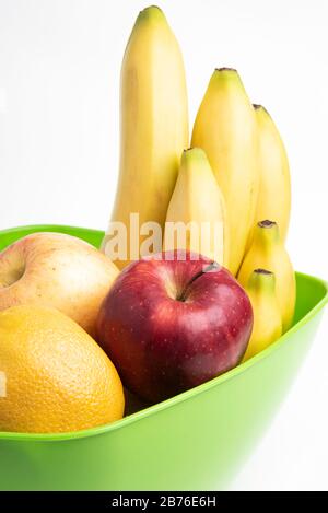Eine leuchtend grüne Plastikschale mit kunstvoll angeordneten frischen und reifen Früchten wie Äpfeln, Bananen, Orangen und anderen auf einem einfarbigen weißen Hintergrund. Stockfoto