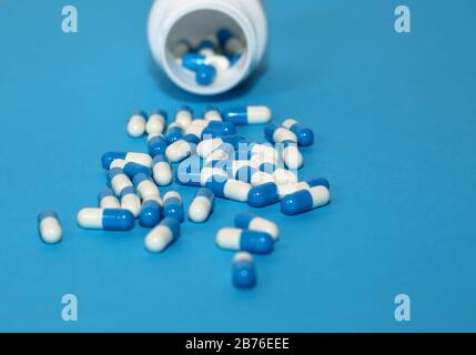Doppelfarbige Pillen Medikamente Tabletten und öffnen pharmazeutische Flasche aus nächster Nähe Auf blauem Hintergrund Stockfoto