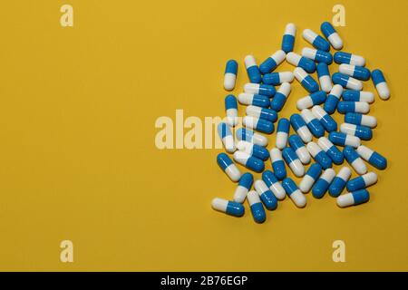 Medikamente Pillen Tabletten Kapseln doppelt farbig weiß-blau Nahaufnahme von oben auf gelbem Hintergrund Stockfoto