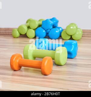 Drei kleine gummierte Hanteln unterschiedlicher Gewichte liegen vor dem Hintergrund von Sätzen der gleichen Hanteln im Hintergrund auf dem Boden Stockfoto