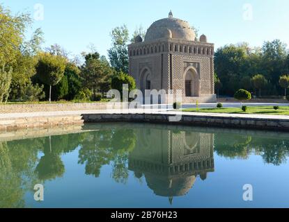 Samanid Mausoleum, das im Wasser in einem Park mit Vegetation in Buchara, Usbekistan reflektiert wird. Ikonisches Beispiel für die frühislamische Architektur in Asien. Stockfoto