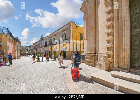 Touristen, darunter ein Mann mit rollendem Koffer, passieren die Kirche des Fegefeuers auf der Piazza Vittorio Veneto in der antiken Stadt Matera, Italien. Stockfoto