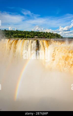 Blick auf einen Teil des Garganta del Diablo im Nationalpark Iguazú mit Regenbogen und einen Teil der brasilianischen Seite des Parks mit vielen Bäumen Stockfoto