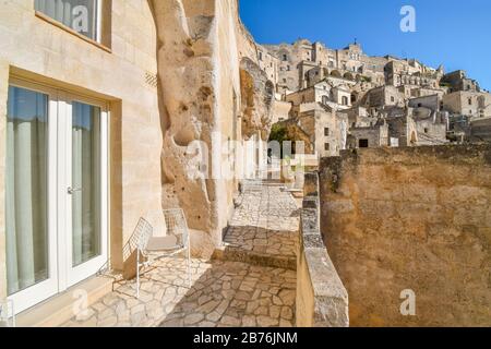 Eine moderne Glasschiebetür und ein Metallstuhl sitzen vor einer Terrasse in der antiken Berghangstadt Matera, Italien. Stockfoto