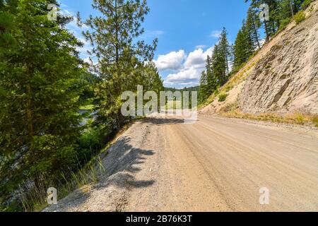 Eine ländliche Schmutzstraße mit einem steilen Berg auf der einen Seite und einer Schlucht auf der anderen Seite in den Bergen des Coeur d'Alene Gebiets in Nord-Idaho, USA. Stockfoto