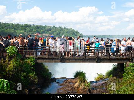 Über den Tourismus an den Iguassu Wasserfällen, Puerto Iguazu, Argentinien wegen der Feiertage. Zahllose Touristen in einer Fußgängerbrücke, die auf die Teufelskehle blickt, fallen. Stockfoto
