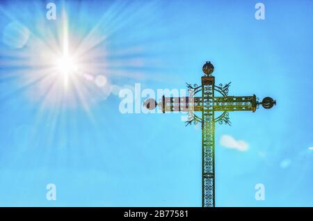 Metallkreuz und ein blauer Himmel mit Sonne scheint Stockfoto