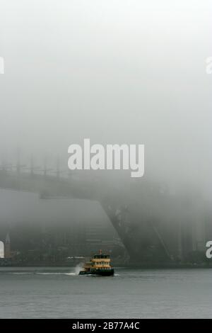 Eine Fähre aus North Sydney führt unter der von dichtem Nebel umgebenen Sydney Harbour Bridge vorbei (eingeschränkte Sicht) New South Wales, Australien. Stockfoto