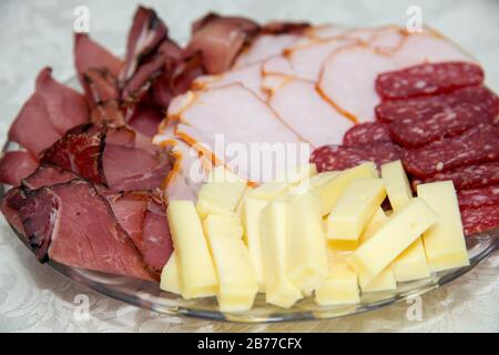 Verschiedene Arten von Fleisch- und Käsesorten, die auf einem Teller über hellem Hintergrund angeordnet sind - selektiver Fokus Stockfoto