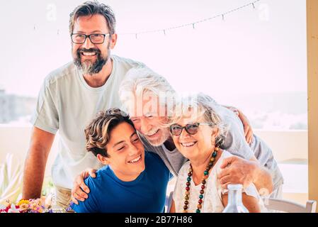 Fröhliche gemischte Familie mit drei Generationen umarmen und gemeinsam genießen - Menschen gruppieren Porträt mit seniod Erwachsene und Teenager zusammen - heller Himmel Hintergrund an Stockfoto