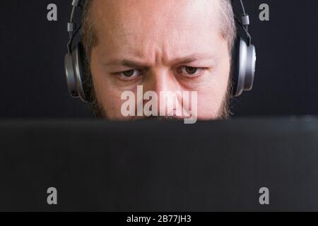 Nahaufnahme des kaukasischen erwachsenen Mannes in Vintage-Pullover und Kopfhörern hinter dem Laptop und Tippen, schwarzer Hintergrund Stockfoto
