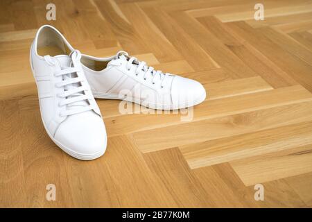 Trendige Sneaker aus weißem Grundleder auf Holzboden Stockfoto