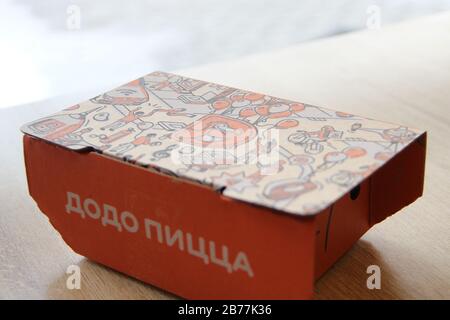 08-02-2020, Russland, Syktyvkar. Orangefarbene Kartonschachtel für Dodo-Snacks mit einer seitlichen Aufschrift Pizza und einem Corporate Design und Logo auf dem Deckel steht auf einem Tisch in einem Restaurant in der Nähe des Fensters. Stockfoto