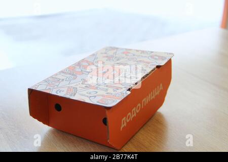 08-02-2020, Russland, Syktyvkar. Orangefarbene Kartonschachtel für Dodo-Snacks mit einer seitlichen Aufschrift Pizza und einem Corporate Design und Logo auf dem Deckel steht auf einem Tisch in einem Restaurant in der Nähe des Fensters. Stockfoto