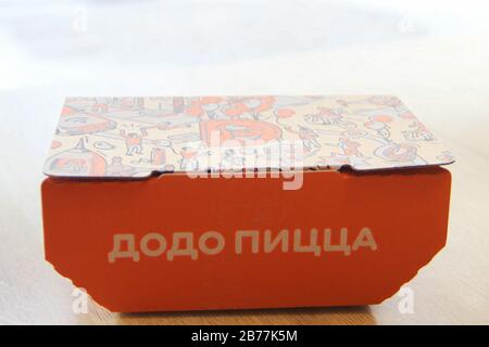 08-02-2020, Russland, Syktyvkar. Orangefarbene Kartonschachtel für Dodo-Snacks mit einer seitlichen Aufschrift Pizza und einem Corporate Design und Logo auf dem Deckel steht auf einem Tisch in einem Restaurant in der Nähe des Fensters. Stockfoto