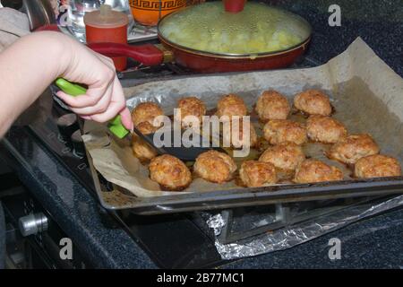 Junge Frau dreht selbstgemachte Schnürchen auf eine Backschnauze. In der Küche im Backofen Fleischbällchen backen Stockfoto