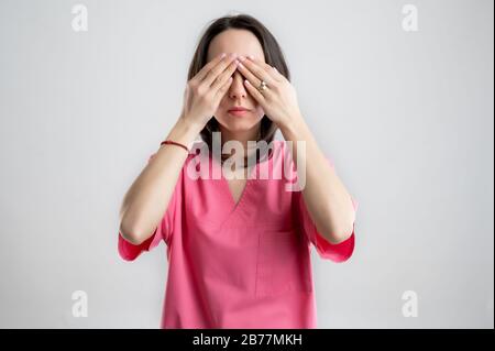 Junge Frau medizinische Fachkrankenschwester oder Ärztin mit rosafarbener Krankenhauskleidung mit braunen Haaren, in der sehen, dass kein Übel auf einer weißen isolierten BA posiert Stockfoto