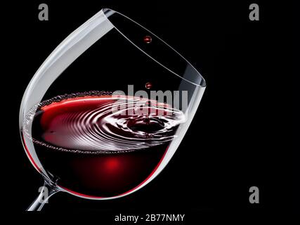 Rotwein in einem Weinglas isoliert auf schwarzem Grund. Tropfen fällt auf die Oberfläche und erzeugt Wellen. Stockfoto