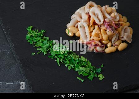 Frische Bohnen und Tintenfische auf schwarzem Steinteller - horizontaler Studioschuss Stockfoto