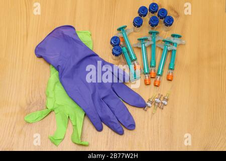 Medizinische Gummihandschuhe neben Fläschchen, Spritzen und Nadeln auf Holzhintergrund Stockfoto