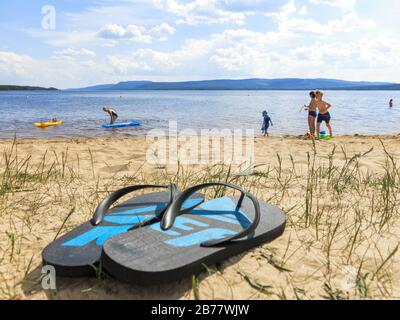 Paar Flip Flops am Strand mit Badelandschaften im Hintergrund. Stockfoto