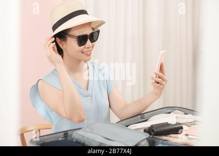 Die Mädchen freuen sich darauf, einen Hut zu wählen, den sie im Urlaub tragen möchten. Sitzen und Sammeln von Kleidung in Taschen, um sich auf Reisen glücklich vorzubereiten. Stockfoto