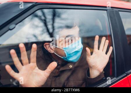 Fahrer, der im Auto sitzt und eine Schutzmaske trägt, ängstigt vor kranken Grippe-Coronavirus-Menschen im Freien. Die Menschen haben Panik. Pandemie Stockfoto