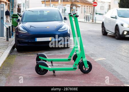 Grüne Elektro-Roller zum Mieten und Laden von Elektroautos, die auf der Stadt geparkt sind. Stockfoto