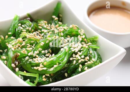 Japanischer Hiyashi-Wakame-Chuka-Salat mit weißen Sesamsamen und Erdnusssoße in einer Schüssel auf weißem Grund. Stockfoto