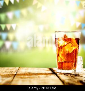 Eistee in einem großen Glas auf Holztisch mit verschwommenem Federhintergrund im Freien. Stockfoto