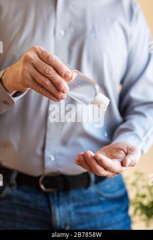 Alkoholgeldesinfektionsmittel aus einer Flasche in die Hände eines Mannes gedrückt, der ein blaues Hemd und eine blaue Freizeitjeans trägt. Selektiver Fokus. Es gibt einen grünen Plan Stockfoto