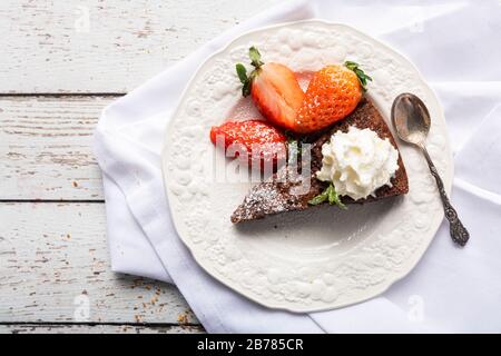 Ein Stück klebriger Schokoladenschlammkuchen, Brownie oder traditionelles schwedisches Kladdkaka auf einem weißen Holztisch mit weißer Serviette im Hintergrund. Der Kuchen Stockfoto