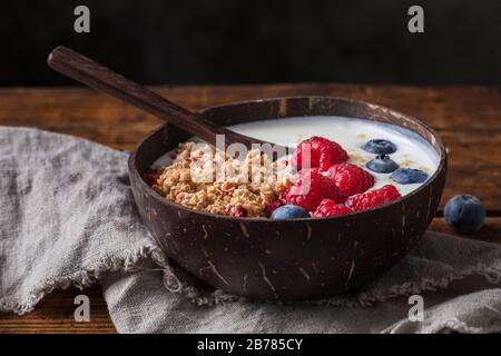 Eine gesunde Frühstücksjoghurt mit Granola, gebufften Quinoa und frischen Blaubeeren und Himbeeren. Das Essen wird in einer natürlichen Kokosschale mit serviert Stockfoto