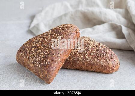 Zwei Stücke gesunder brauner Brotbrötchen. Die dreieck geformten Brote sind mit Flachssamen und Sesamsamen bedeckt. Stockfoto