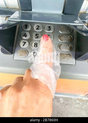 Coronavirus und Bargeld. Frau drückt einen Finger auf einen Geldautomaten. Verwenden Sie eine Plastiktüte oder Handschuhe an der Hand, um Viren, Keime, Bakterien von schmutzigen Geldautomaten zu vermeiden. Stockfoto