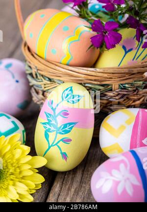 Nahaufnahme von bunten ostereiern auf Holztisch und in einem Korb mit schönen Blumen Stockfoto