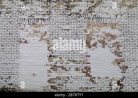 Eine Mauer aus Backstein mit versperrten Fenstern, die weiß und verblasst sind Stockfoto